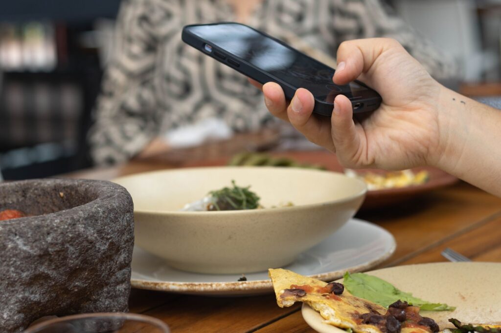 pessoa fotografando prato de restaurante com celular próximo à janela